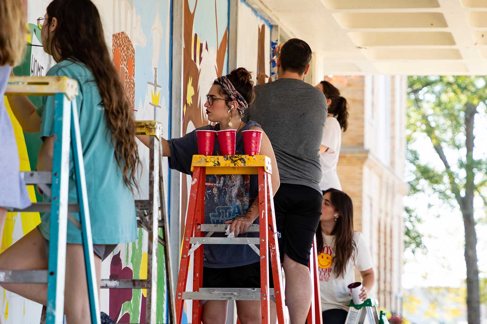 students on ladders painting