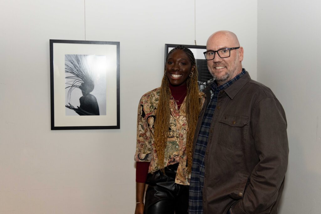(l to r) FHU student Angelina Barr and FHU Associate Professor of Art Jud Davis stand next to a photo from her series “I Am Not My Hair.”