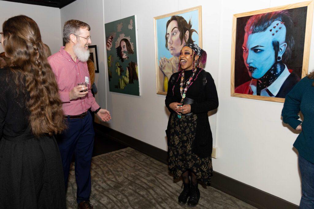 FHU student Leilani Baker shares a laugh with guests while standing in front of her piece called “Motionless.”