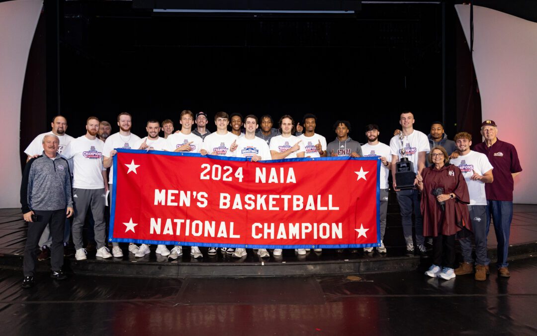FHU Men's Basketball Team hold the championship banner Tuesday, April 2, 2024, in Loyd Auditorium following a special celebration of their historic win