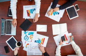 A team of experts working together with documents, notebooks, and devices spread across a conference table