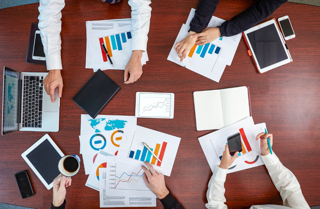 A team of experts working together with documents, notebooks, and devices spread across a conference table