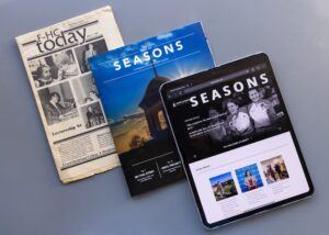 Three publications are displayed on a gray surface: a black-and-white newspaper, a glossy magazine titled SEASONS, and a tablet showing a digital version of the magazine with images and a black-themed interface.