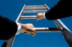 A person in a suit climbs a metal ladder against a clear blue sky, viewed from below, with both hands gripping the rungs.