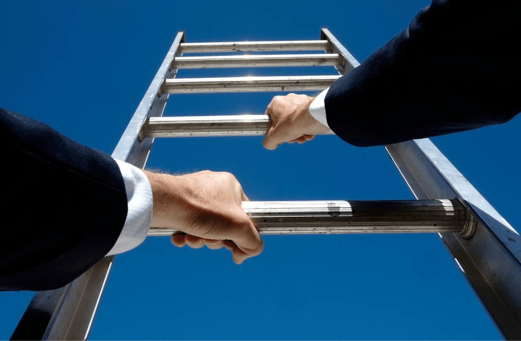 A person in a suit climbs a metal ladder against a clear blue sky, viewed from below, with both hands gripping the rungs.