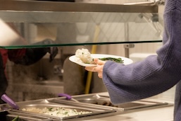 A woman hands a student a plate of food in the dining hall on campus