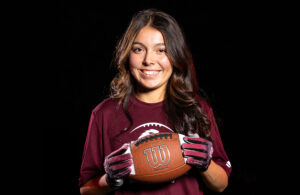 Young girl with long brown hair holding football and smiling