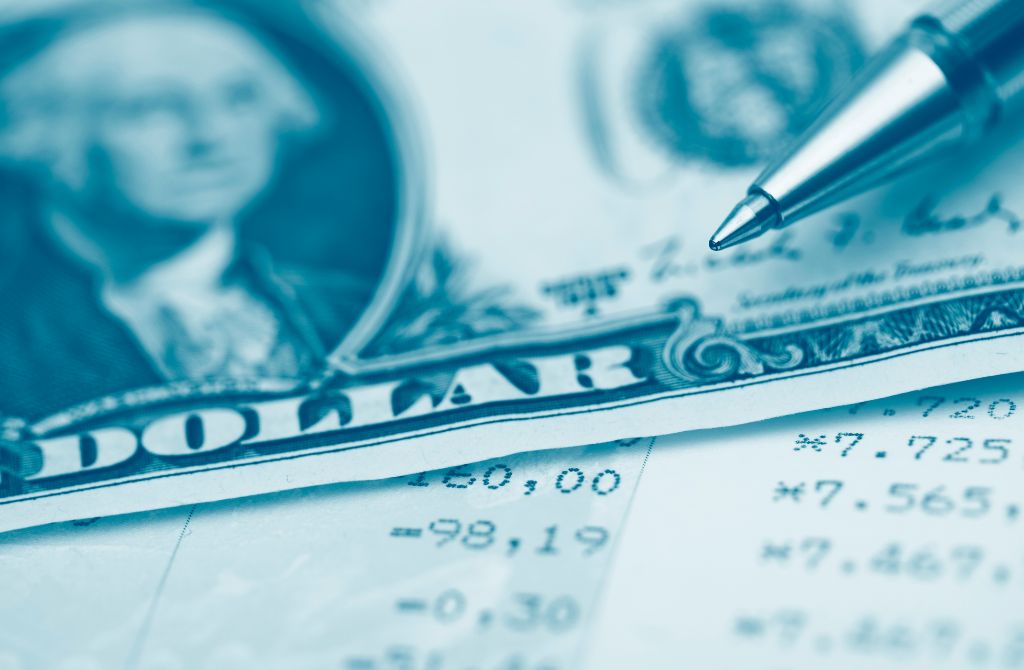 Close-up of a pen resting on a printed financial statement, with a partial view of a U.S. dollar bill in the background, symbolizing finance, budgeting, or accounting.