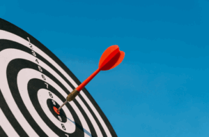 A red dart is sticking in the red bullseye of a black and white target