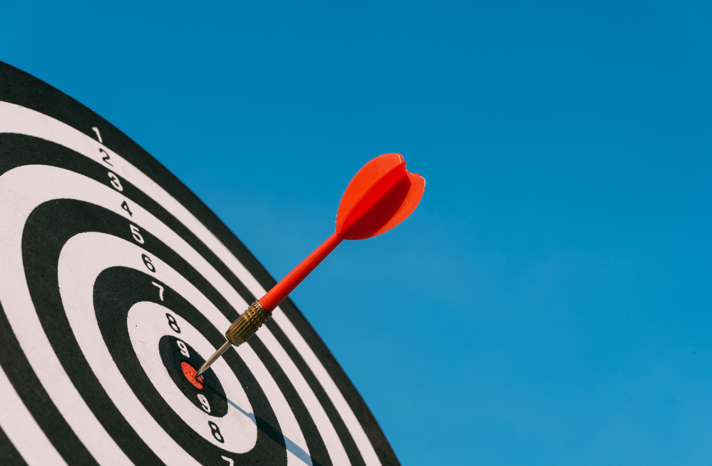 A red dart is sticking in the red bullseye of a black and white target