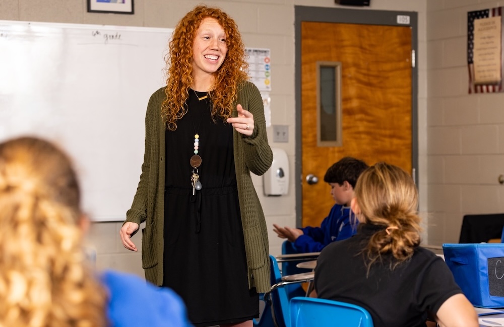 A woman stands in front of her class and teaches a lesson