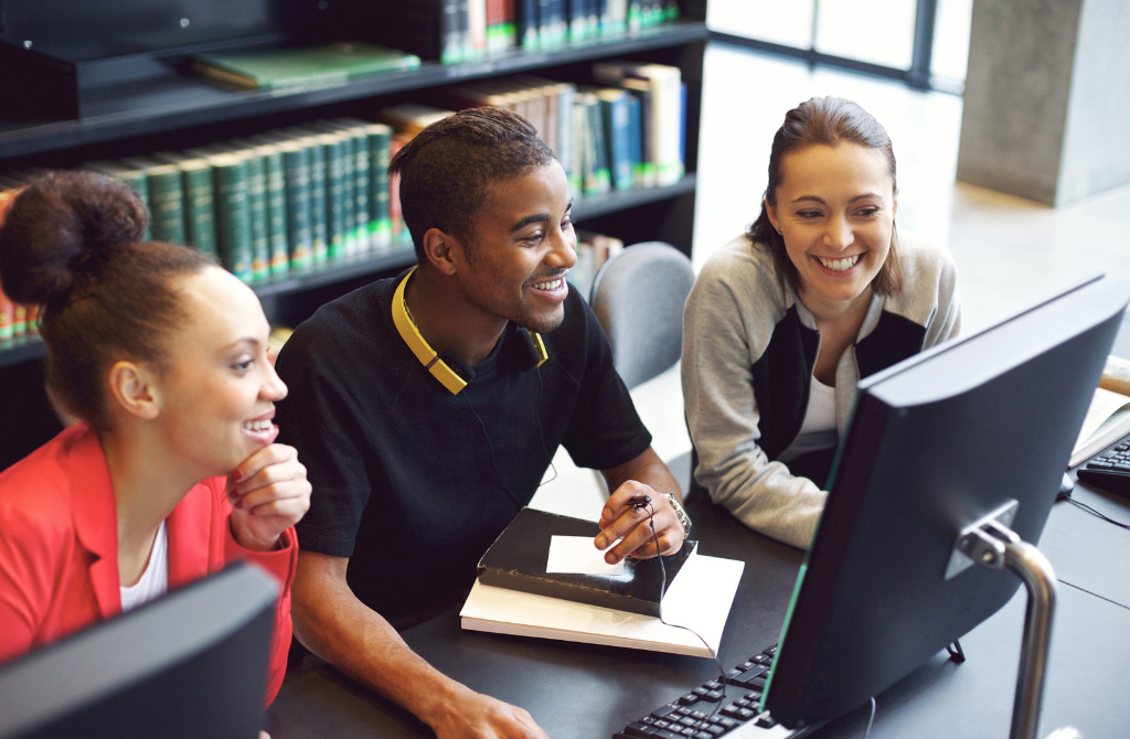 A group smiles at the computer monitor as they work on a group project
