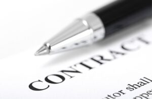 A close-up of a pen resting on a document with the word CONTRACT printed in bold letters, suggesting the signing or review of an agreement.