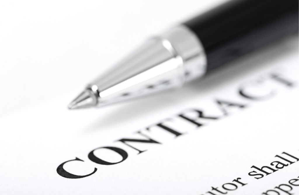 A close-up of a pen resting on a document with the word CONTRACT printed in bold letters, suggesting the signing or review of an agreement.