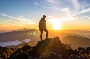 A man looks at the sunset as he stands atop a mountain